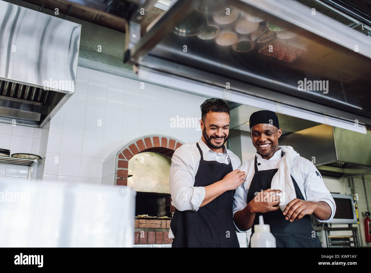 Sorridente chef professionisti che lavorano in ristorante cucina. Chef Felice in uniforme e grembiule in cucina commerciale. Foto Stock