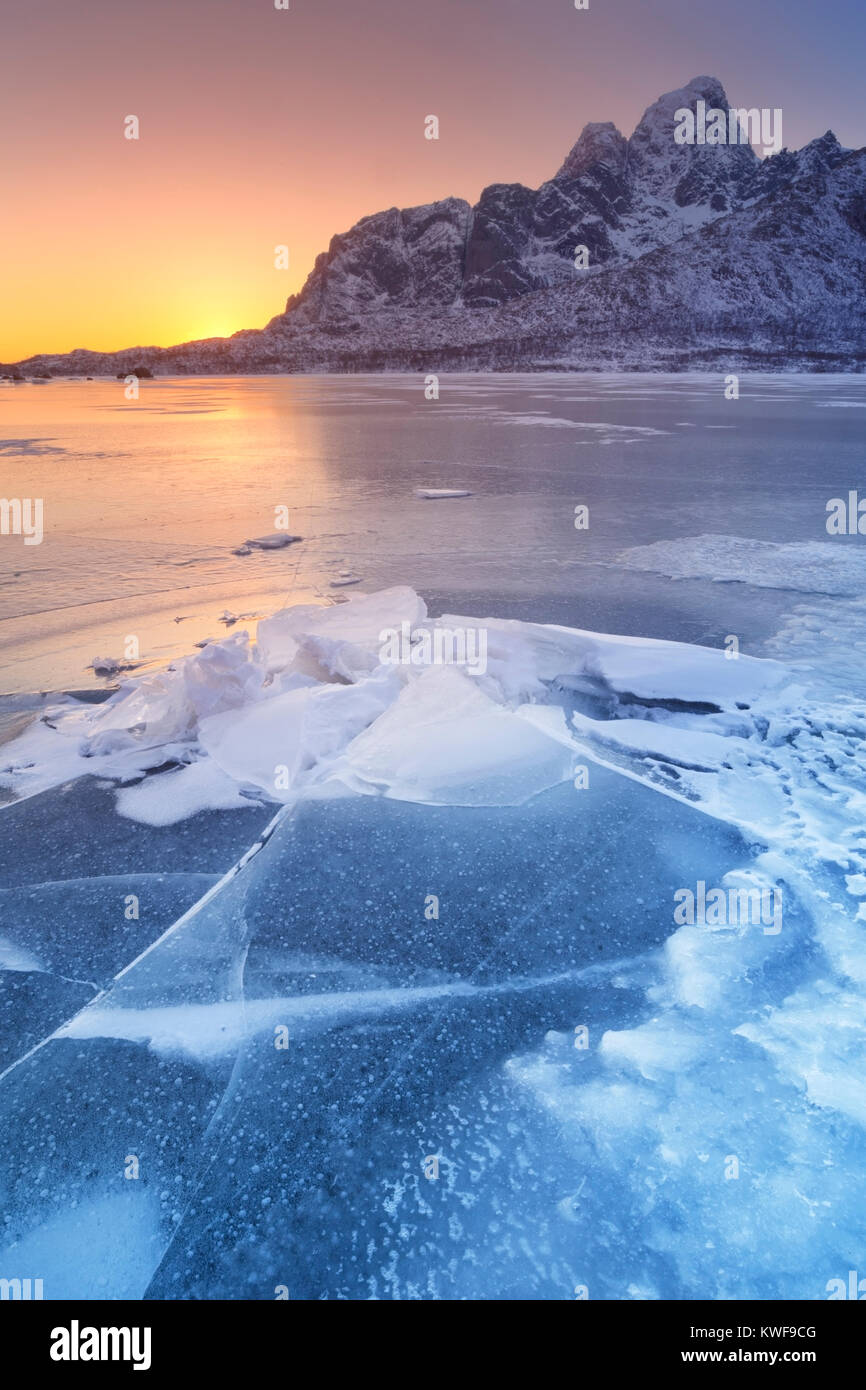 Un fiordo congelato sulle Lofoten in Norvegia settentrionale con il basso sole di mezzogiorno dietro le montagne. Foto Stock