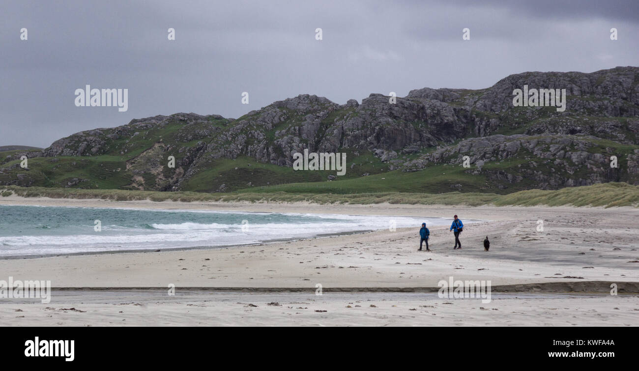 Due persone e un cane camminare sotto cieli grigi sulla spiaggia Reef, isola di Lewis, Ebridi Esterne, Scozia Foto Stock