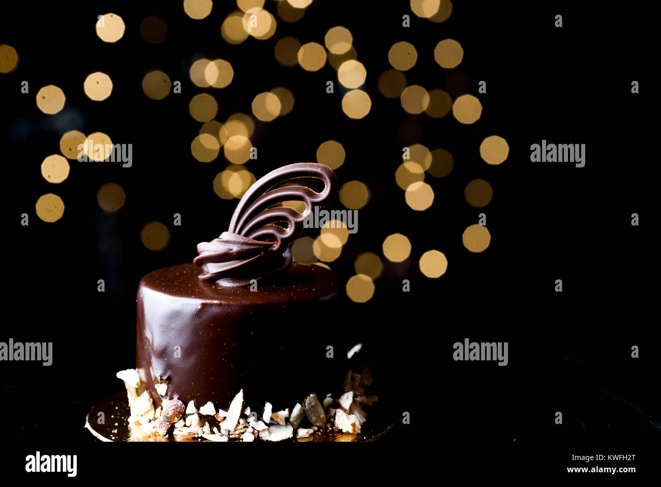 Orizzontale basso studio chiave accesa cioccolato torta gnache con bordo di mandorle tritate e delicate decorazioni scolpite sulla parte superiore. Foto Stock