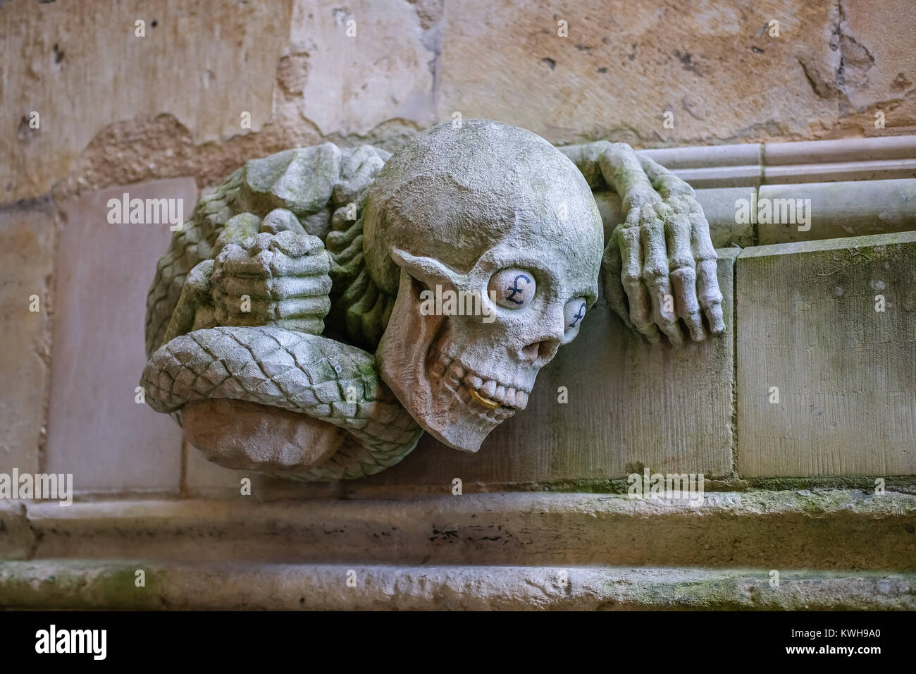 La scultura contemporanea di un serpente dotato di mani umane e il cranio completo con una moneta d'oro tra i suoi denti e £ segno occhi alla Cattedrale di Lincoln Foto Stock