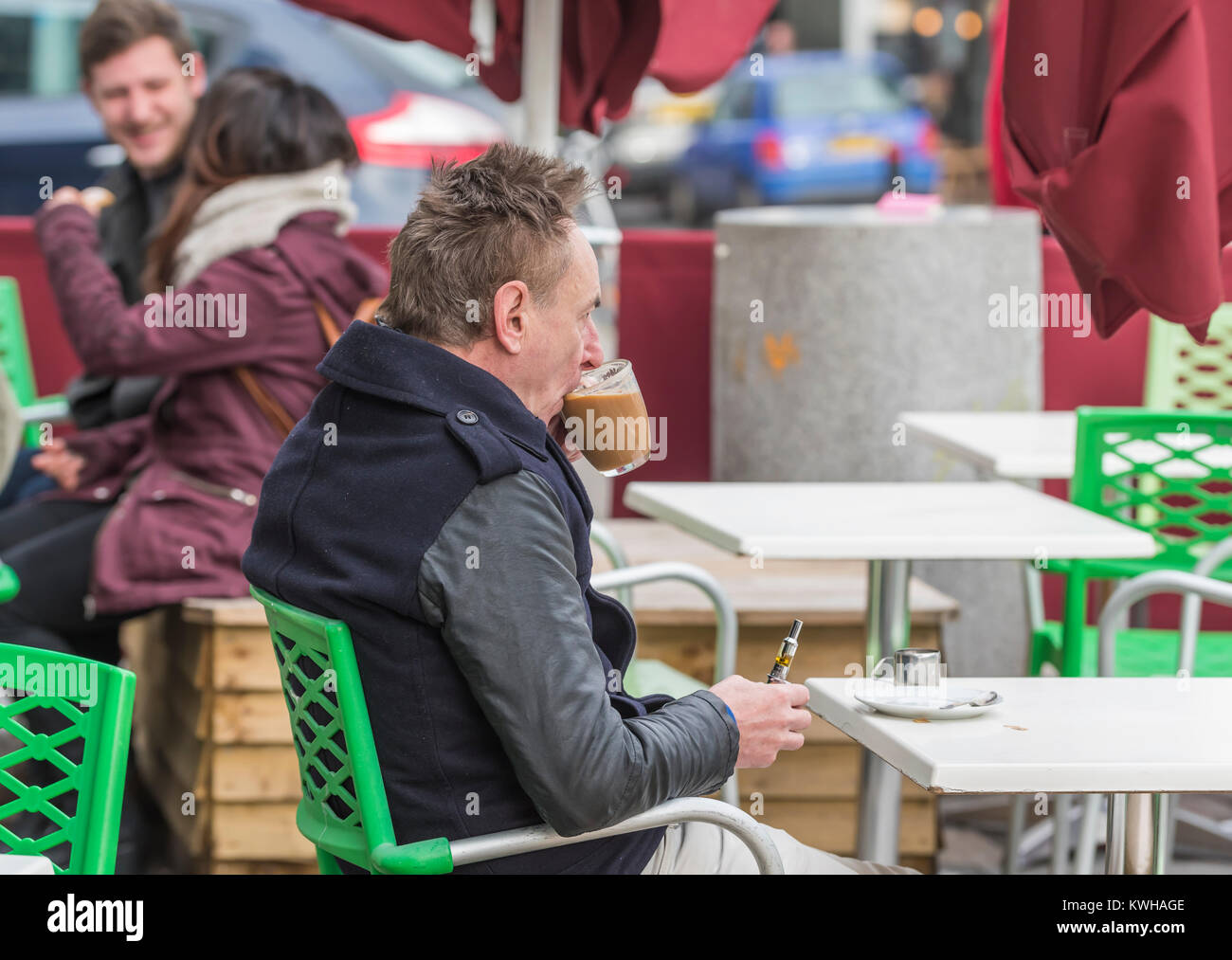 Uomo seduto in un bar al di fuori in inverno avente una bevanda calda di caffè, in Inghilterra, Regno Unito. Foto Stock