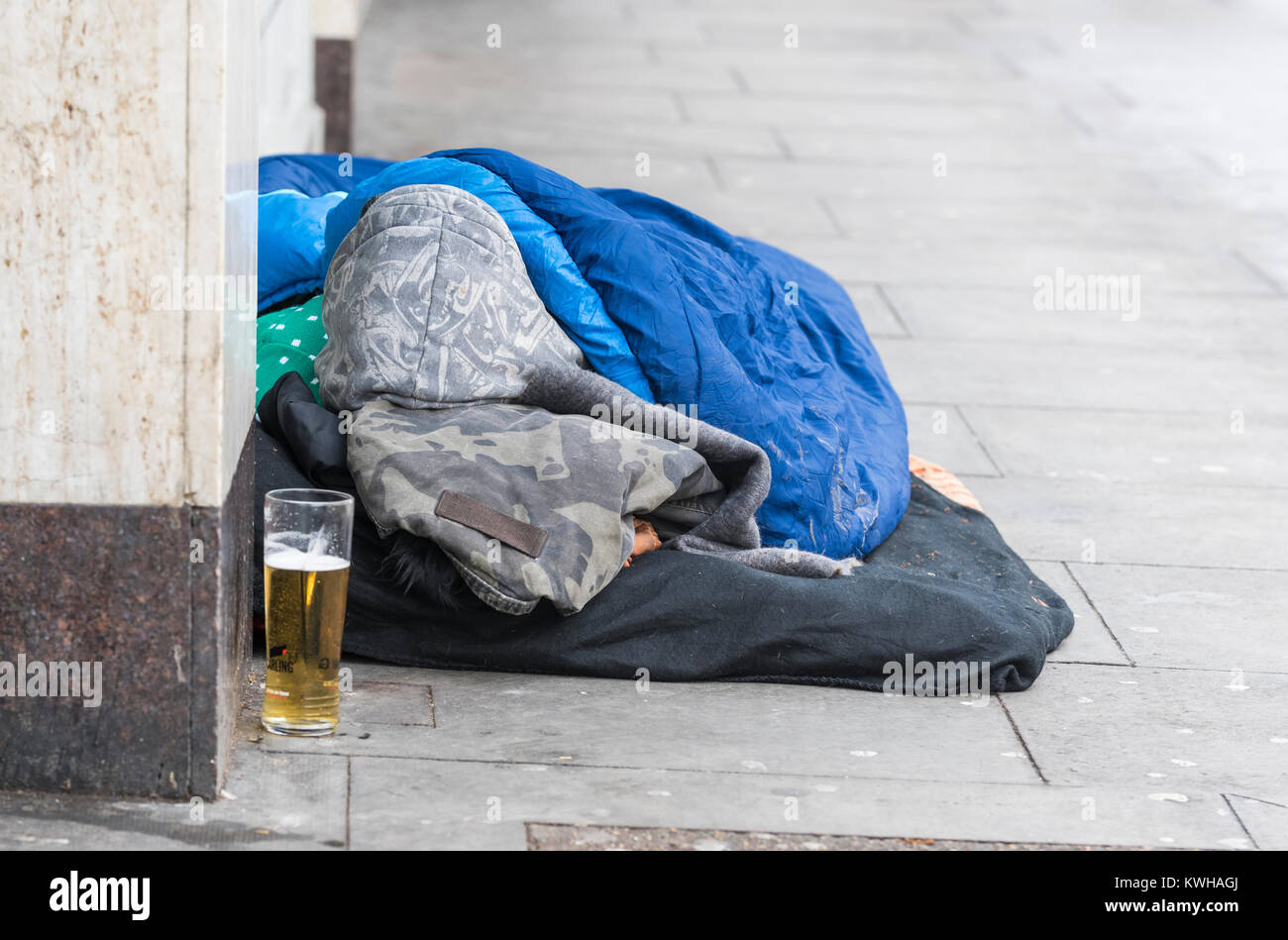 La persona senza dimora di dormire su strade con un parzialmente bevuto bicchiere di lager (alcool) vicino a Brighton, East Sussex, Inghilterra, Regno Unito. Foto Stock