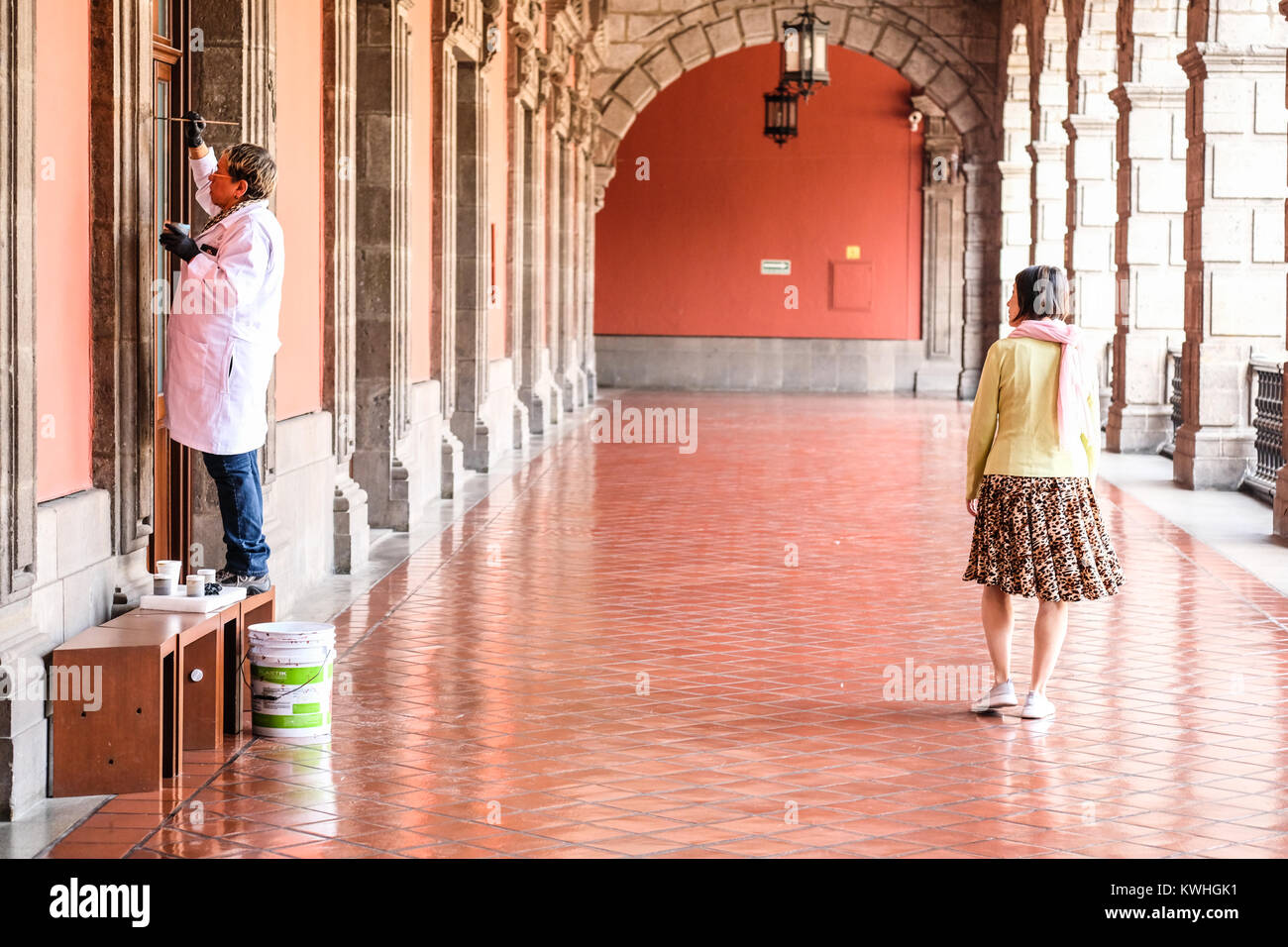 Un equipaggio di restauro vernice su un muro in Plaza de la Constitcion a Città del Messico con un turista femminile passando da Foto Stock