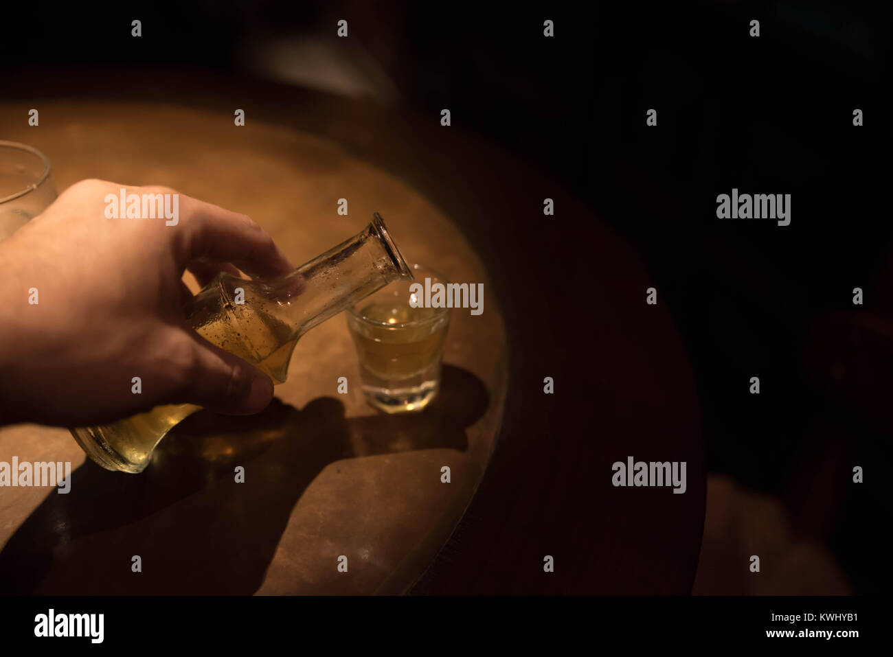 Il riempimento di uno snap shot con tradizionale greco (rakomelo raki con miele) in un tavolo di legno con luce scarsa Foto Stock