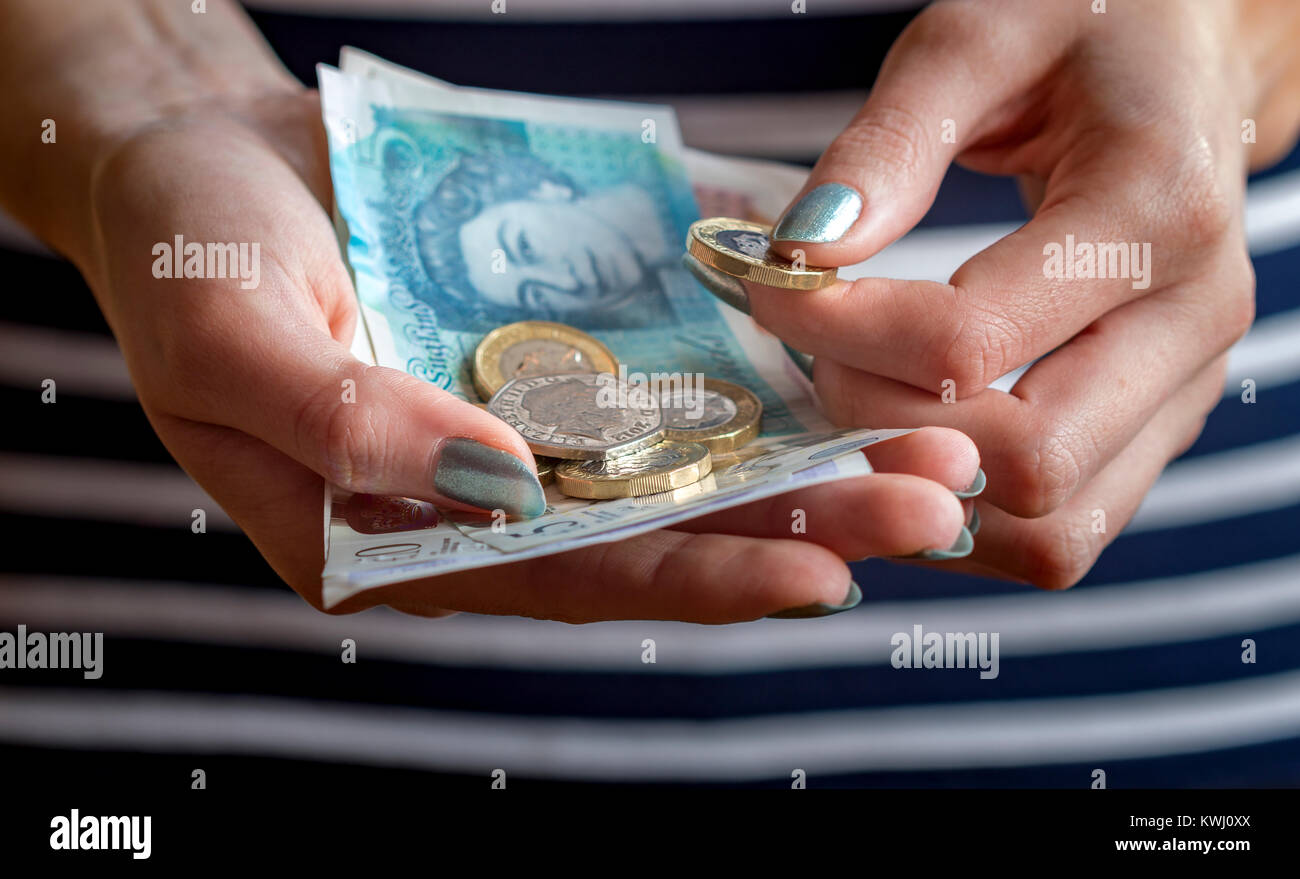Primo piano delle mani di una donna in possesso di contanti, con banconote e monete di varie denominazioni di valuta britannica. Foto Stock