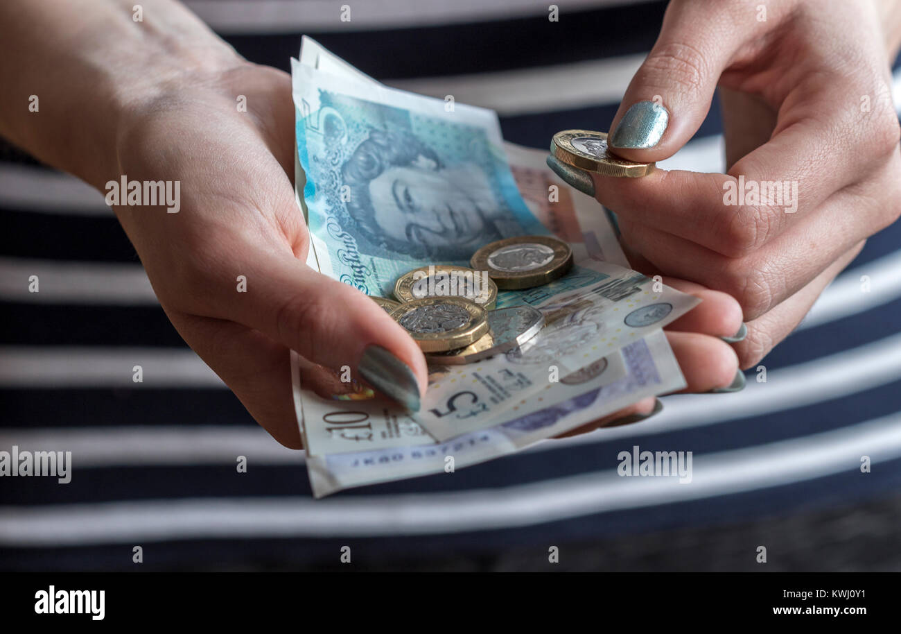 Primo piano delle mani di una donna in possesso di contanti, con banconote e monete di varie denominazioni di valuta britannica. Foto Stock