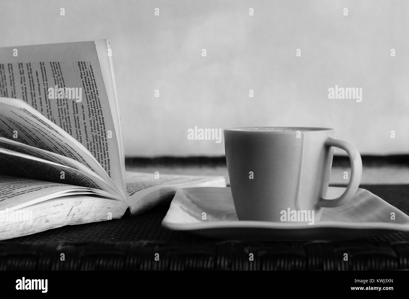 Immagine in bianco e nero di una tazza di caffè o di tè mantenuta oltre un libro aperto con le pagine svolazzanti. Foto Stock
