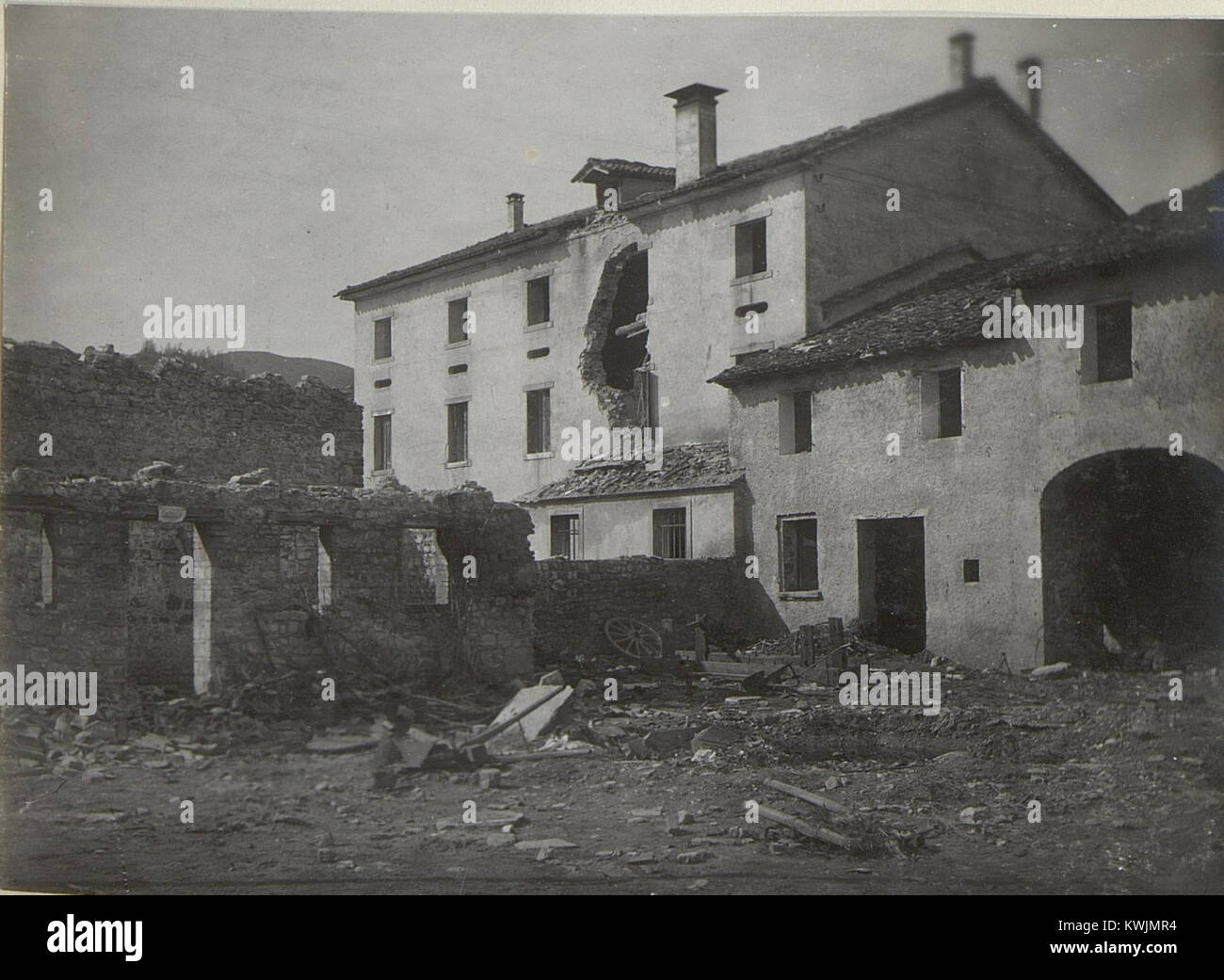 Questa fotografia riporta le conseguenze della distruzione delle case nel villaggio di Giusin, illustrando i danni strutturali agli edifici residenziali probabilmente associati all'attività bellica. L'immagine fa parte di un archivio storico che documenta l'impatto dell'edilizia abitativa civile e il cambiamento di insediamento regionale durante un periodo di conflitto. Foto Stock