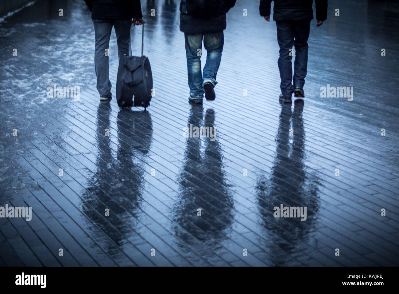 Tre persone a piedi lungo una passerella di bagnato le loro riflessioni appeso al di sotto di esse Foto Stock