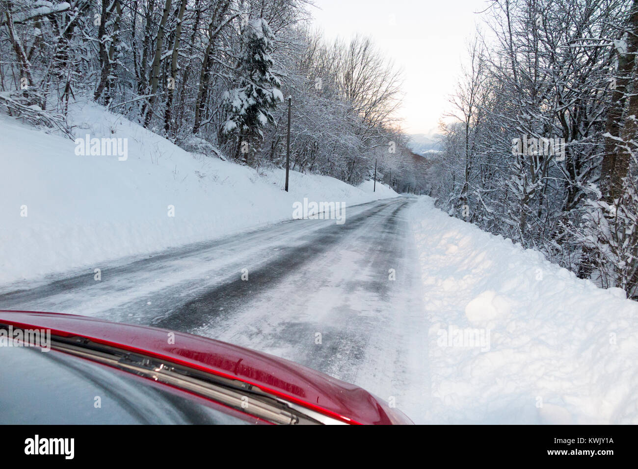 Icy scivoloso coperta di neve francese paese alpino road, con ghiaccio, dopo una bufera di neve, visibile attraverso il parabrezza dall'interno dell'auto al tramonto. Alpi Francia Foto Stock