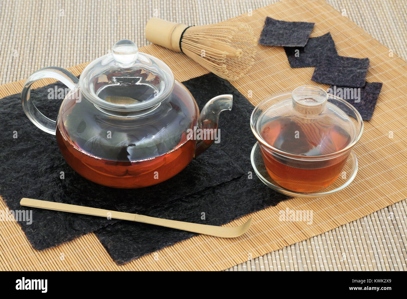 Il giapponese nori alghe salute tè bere con vetro teiera e tazza da tè, fogli essiccati, frusta e agitatore su sfondo di bambù. Pieno di sano minerali. Foto Stock