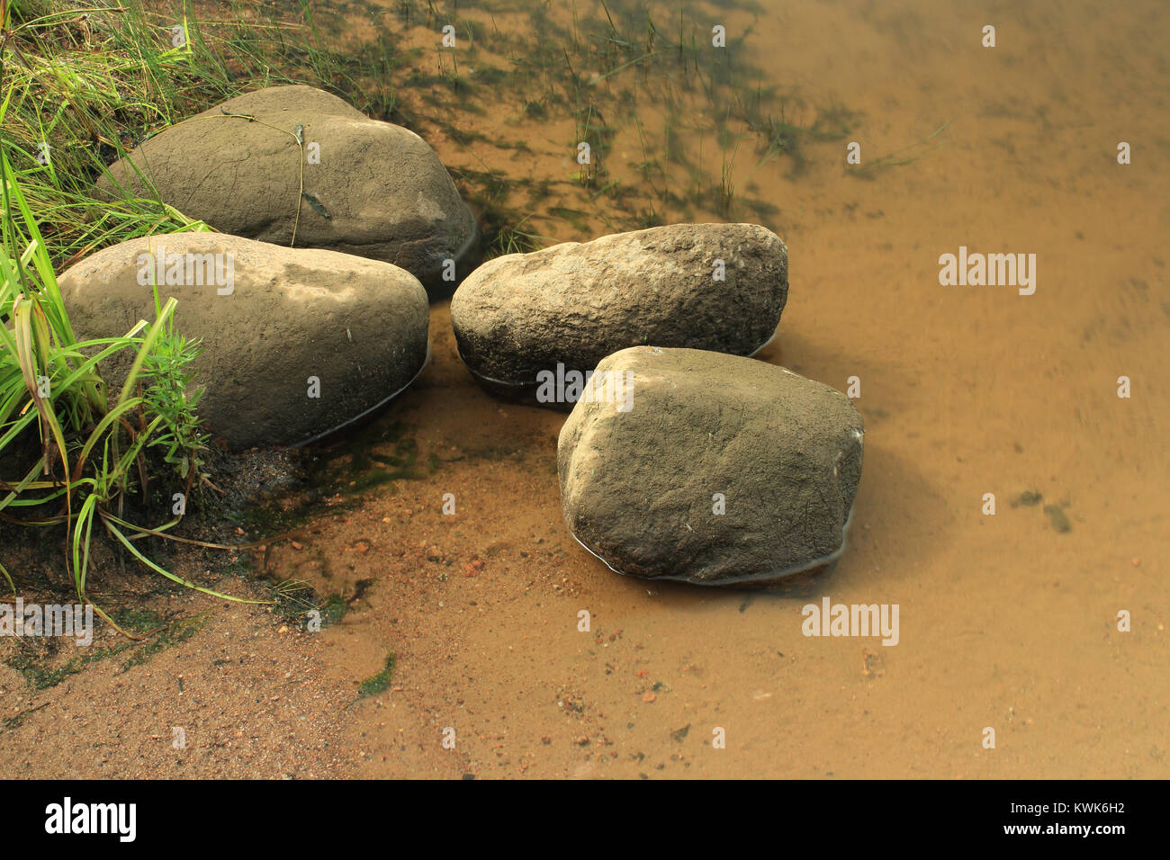 Massi liscia risiede nell'acqua sulla banca del fiume di bassa marea, una lunga esposizione Foto Stock