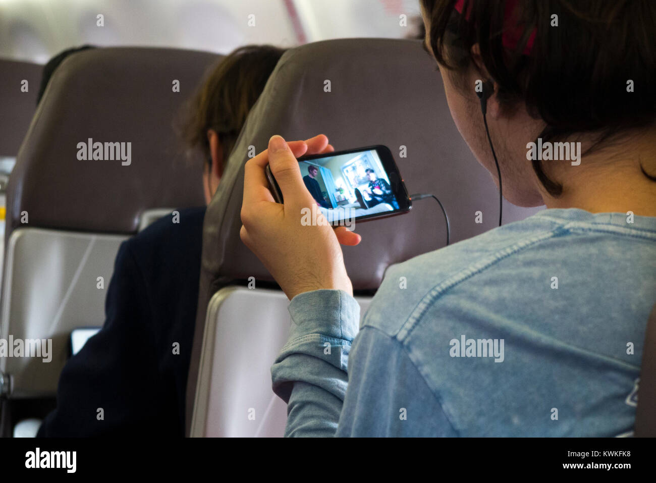 Passeggero maschio giocando un visualizza filmato, film o programma televisivo sul suo telefono cellulare - attiva la modalità di uso in aereo, su Embraer aereo / aeroplano / Aereo Foto Stock