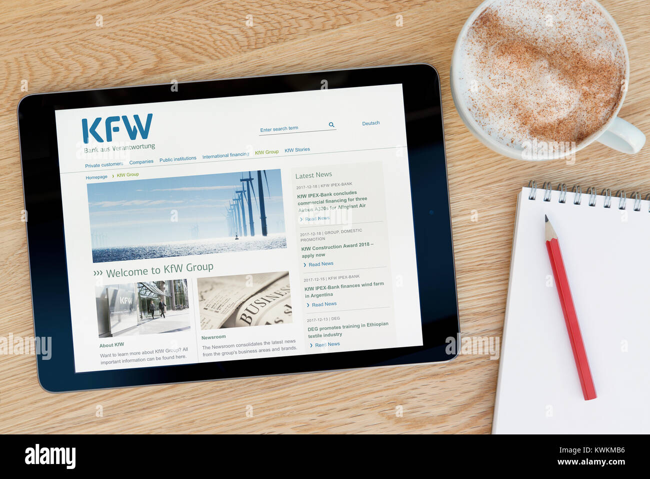 La KfW Gruppo sito web su un iPad dispositivo tablet, appoggiato su un tavolo di legno accanto a un blocco note, matita e tazza di caffè (editoriale solo) Foto Stock