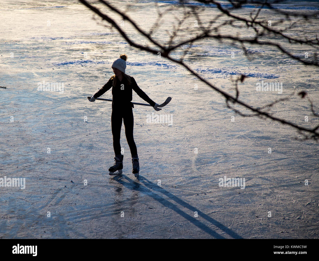 Silhouette di una giovane ragazza a giocare a hockey su un laghetto congelato Foto Stock