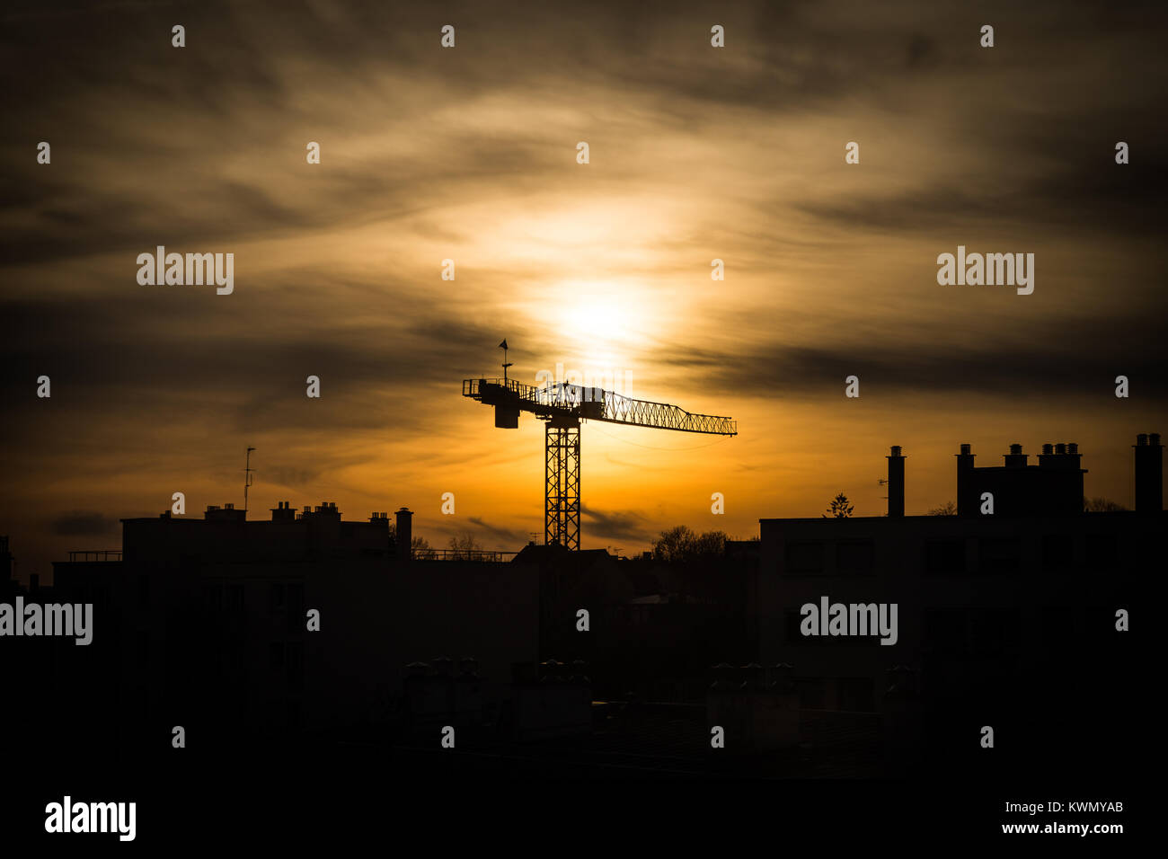 Grandi gru industriali stagliano al tramonto contro un cielo arancione che salgono sopra i tetti di una città sulla skyline Foto Stock