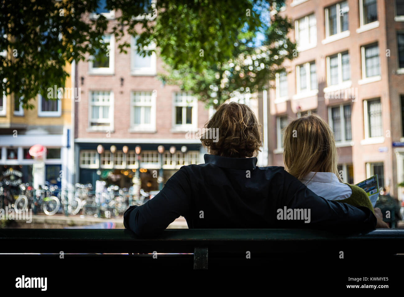 Coppia romantica seduta a braccetto su un banco di urbano che si affaccia su case a schiera con le biciclette parcheggiate al di sotto guardando dalla parte posteriore Foto Stock