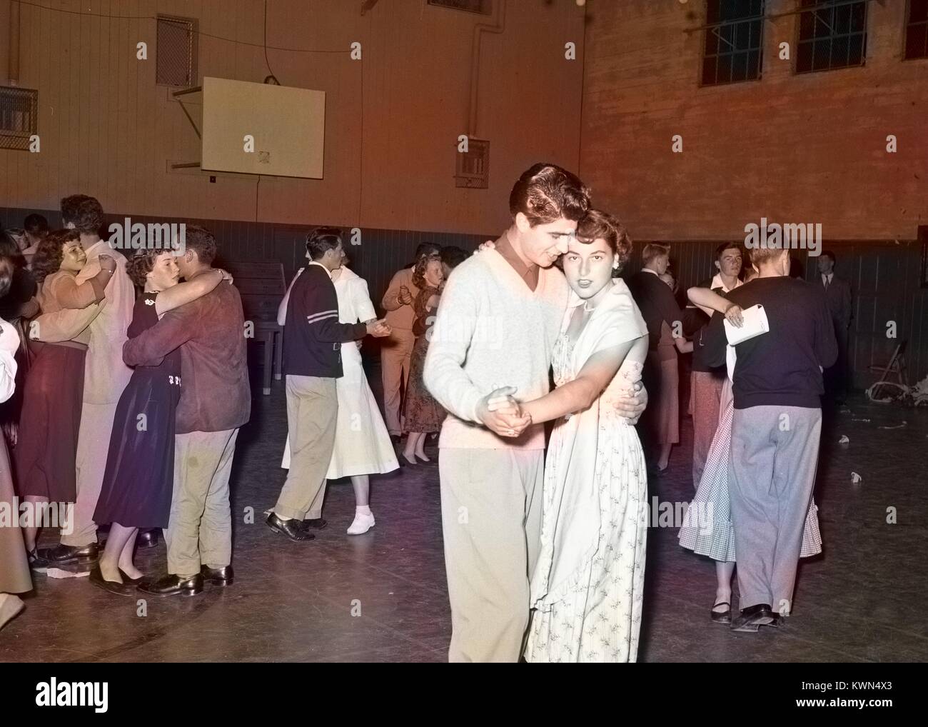 Un giovane uomo e donna giovane tenere mani mentre slow dancing durante una alta scuola di danza nella palestra a Monterey unione di alta scuola, mentre altre coppie danza in background, Monterey, California, 1950. Nota: l'immagine è stato colorizzato digitalmente usando un processo moderno. I colori possono non essere periodo-precisa. Foto Stock