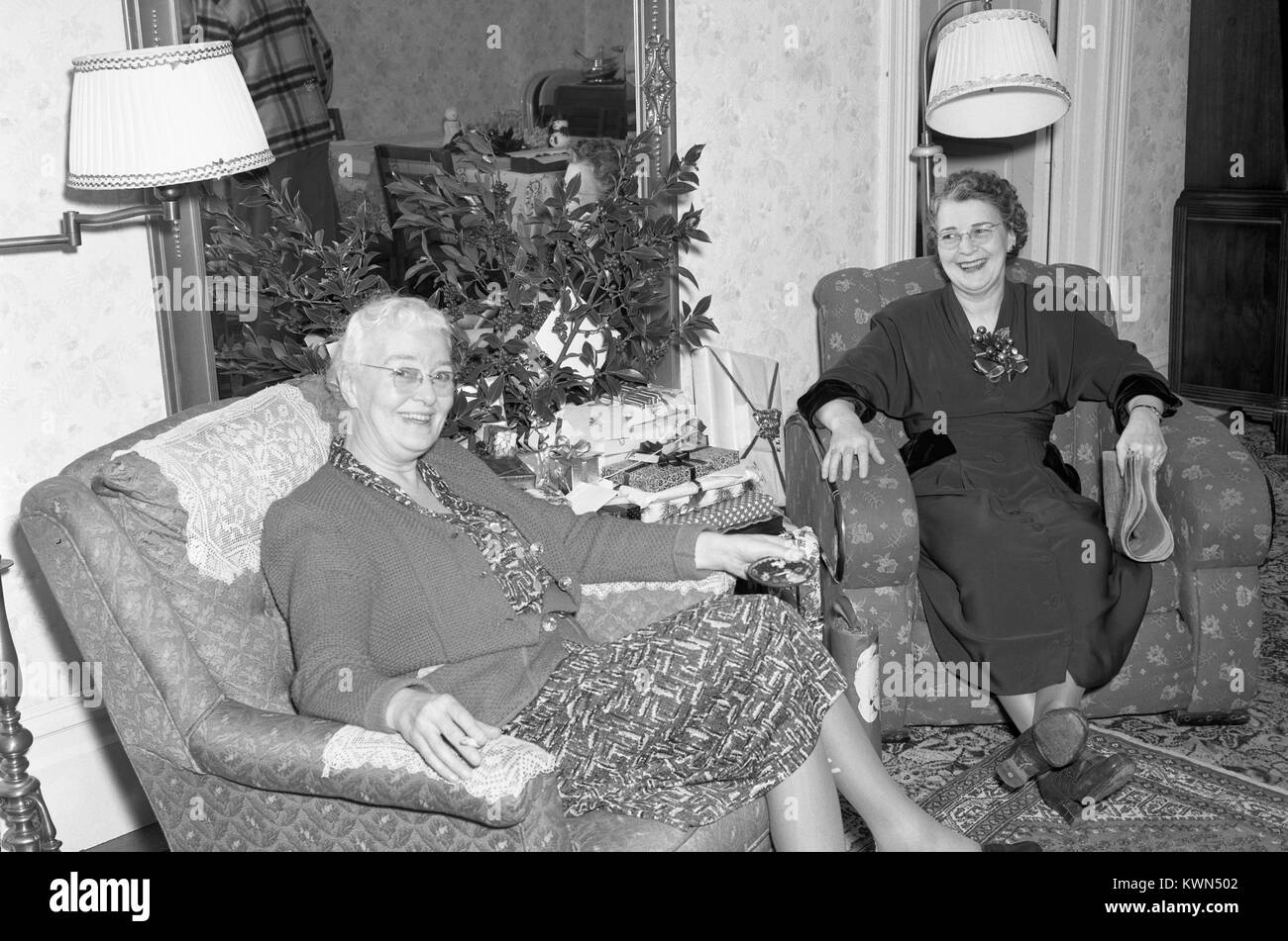 Due donne mature sedere sulle sedie nel salotto di una casa suburbana, entrambi sorridenti, Eureka, California, 1950. Foto Stock