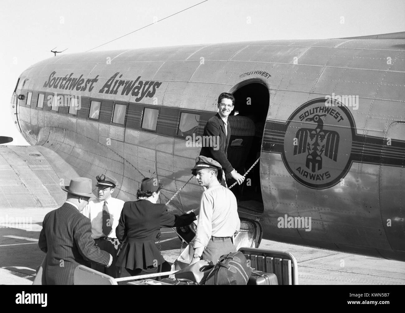 Un giovane uomo sorrisi come egli assi un Southwest Airways aerei ad elica, come una coppia matura prepara anche a bordo e un portiere si erge da con un carrello che porta bagagli, Monterey, California, 1950. Southwest Airways è stato uno dei primi a sconto regionale carrier serve la California e Oregon, ed era noto per i suoi servizi senza fronzoli ed estremamente veloci tempi di imbarco. Foto Stock