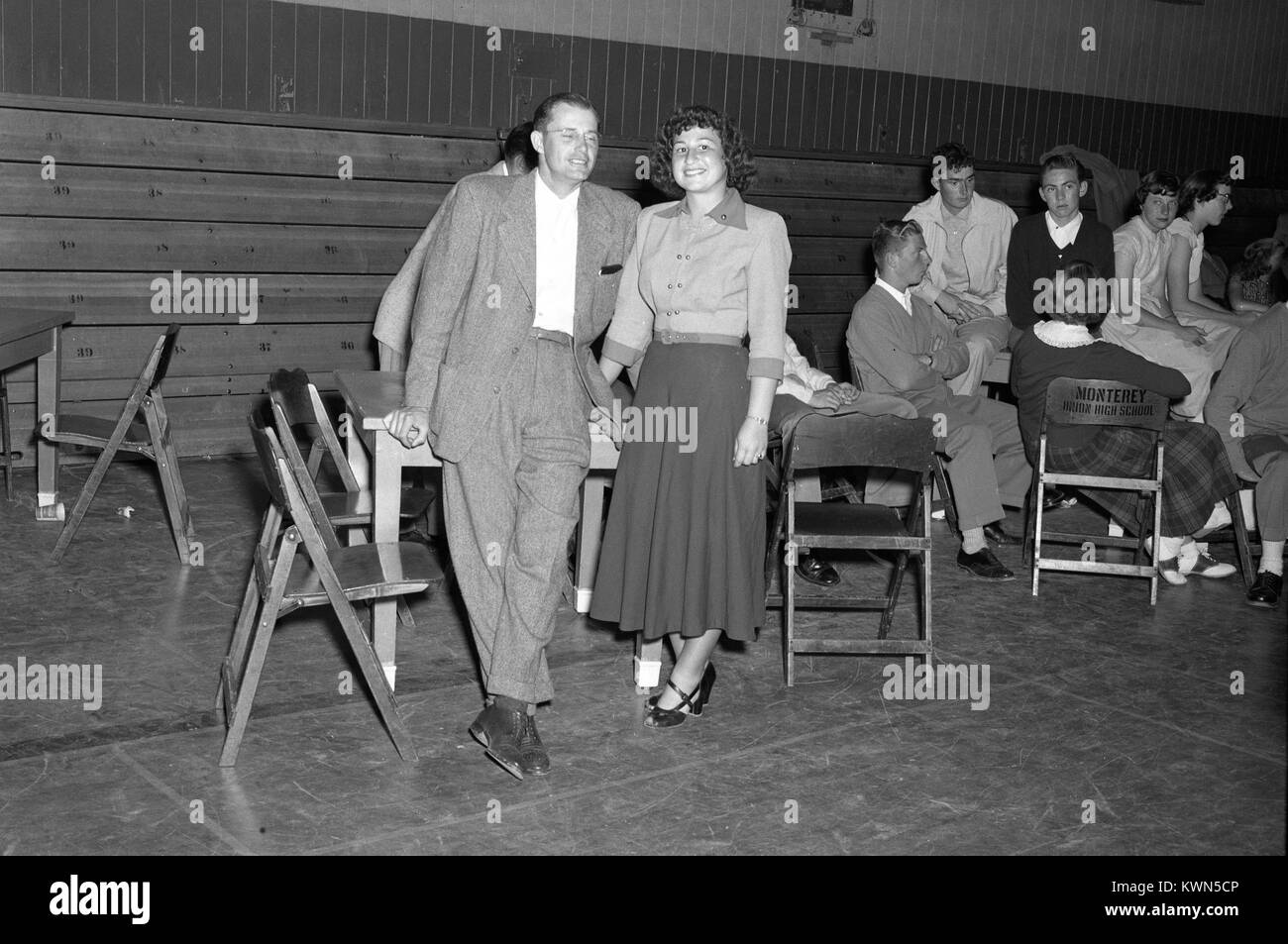 Un padre sorrisi e pone con sua figlia mentre agisce come suo accompagnatore durante una alta scuola di danza, come altri giovani sedere ai tavoli in background, a Monterey Unione High School, Monterey, California, 1950. Foto Stock