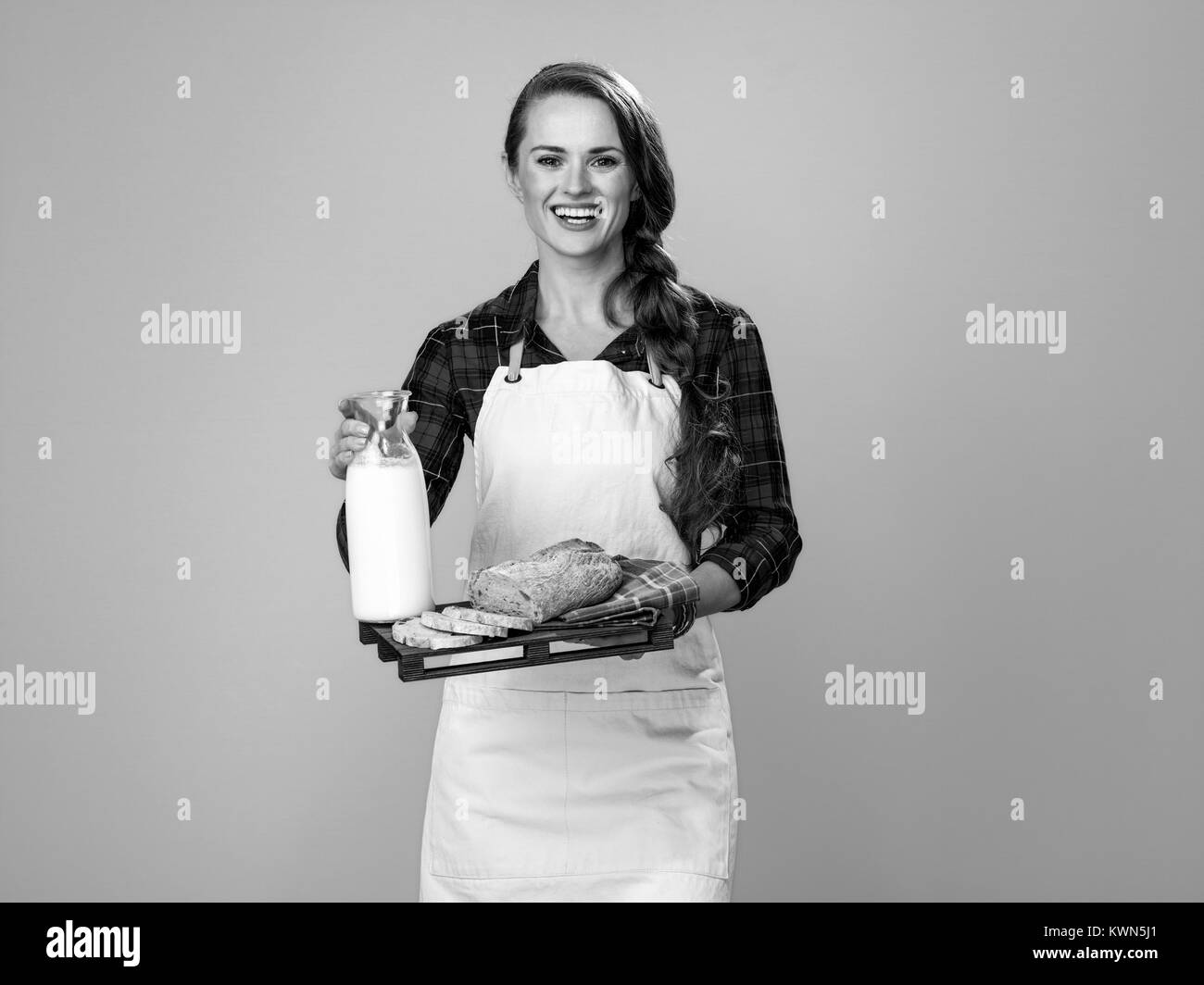 Cibo sano per il vostro tavolo. Ritratto di sorridente donna moderno agricoltore indossando il grembiule su sfondo giallo che mostra fette di pane e latte fresco su un vassoio Foto Stock