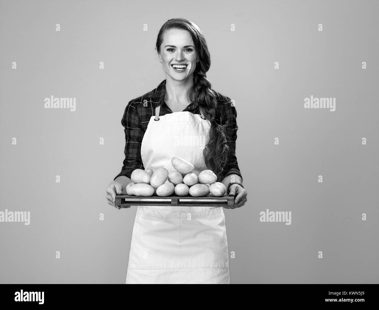 Cibo sano per il vostro tavolo. Ritratto di felice giovane donna cucinare indossando il grembiule isolato su giallo che mostra le patate Foto Stock