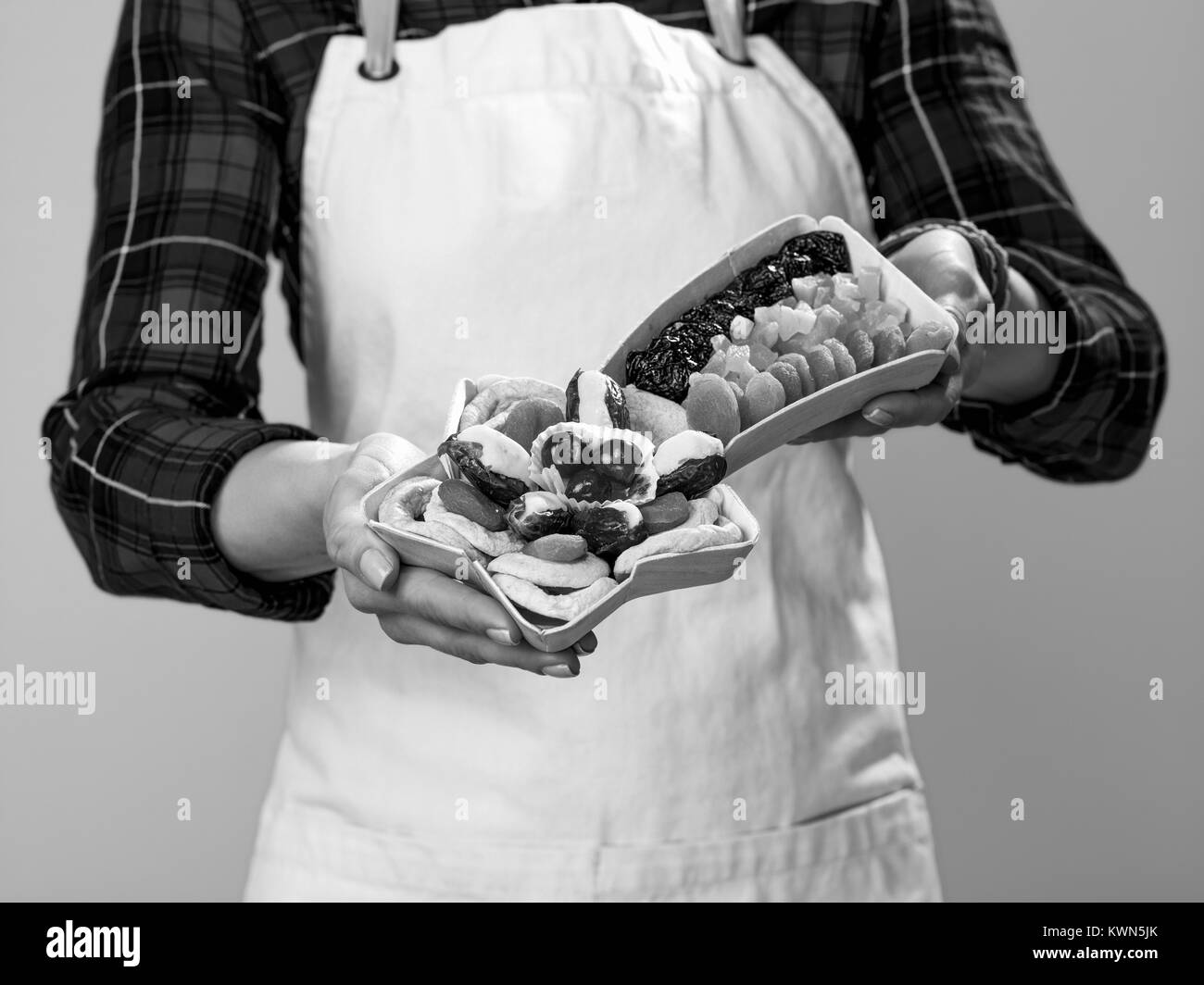 Cibo sano per il vostro tavolo. Primo piano sulla donna giovane agricoltore che indossa il grembiule su sfondo giallo che mostra il Natale Pranzo frutta secca Foto Stock