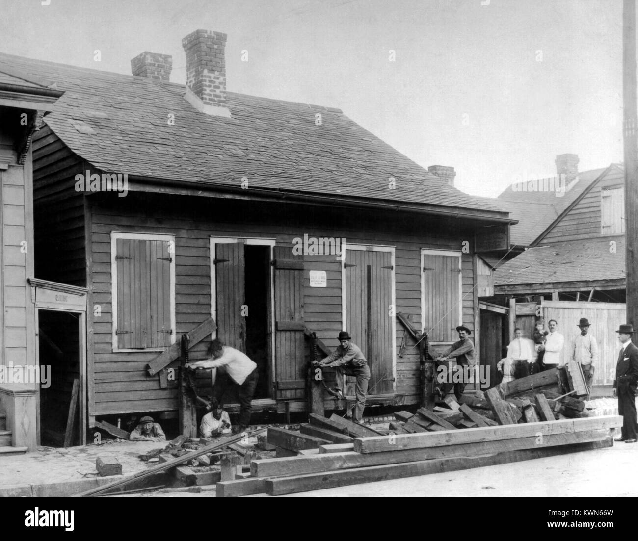 Lavoratori utilizzando martinetti manuale per sollevare una piccola casa fuori dalla sua fondazione nel corso di un progetto di costruzione, 1914. Immagine cortesia CDC. () Foto Stock