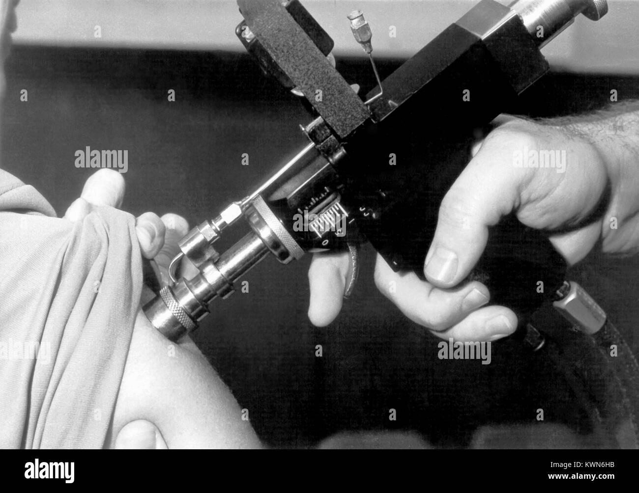 Questa fotografia mostra un medico utilizzando un iniettore a getto pistola durante un adulto programma di immunizzazione, 1958. Un iniettore a getto è un dispositivo che utilizza la pressione gassosa per la propulsione di farmaci o vaccini attraverso gli strati esterni della cute e nella sottostante i tessuti sottocutanei. Questa operazione viene realizzata senza l'uso di aghi. Immagine cortesia CDC. Foto Stock