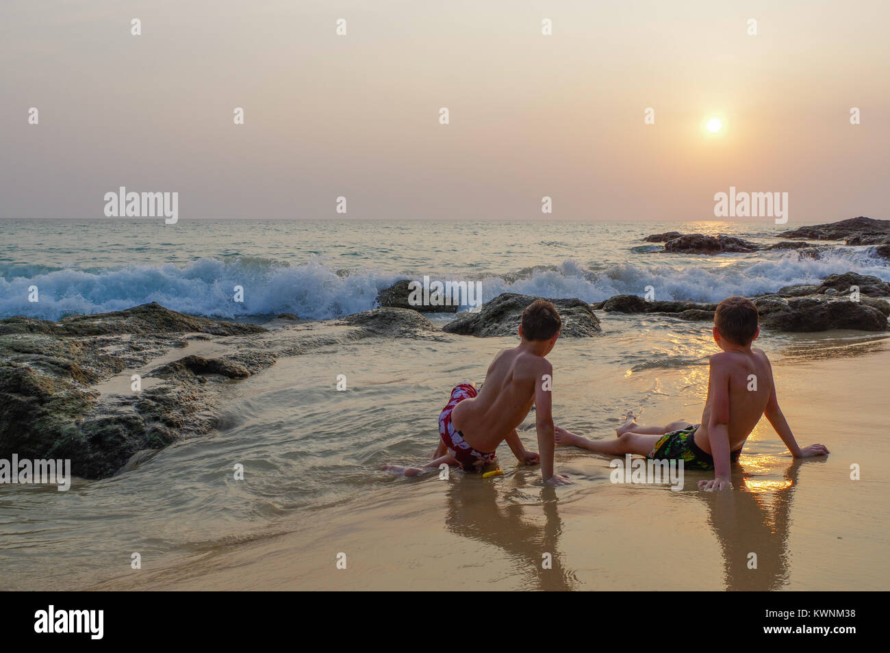 Due Ragazzi Seduto Sulla Spiaggia In Riva Al Mare E Godersi Il Tramonto Dietro Le Rocce Ed Il Mare Thailandia Isola Di Phuket Surin Foto Stock Alamy