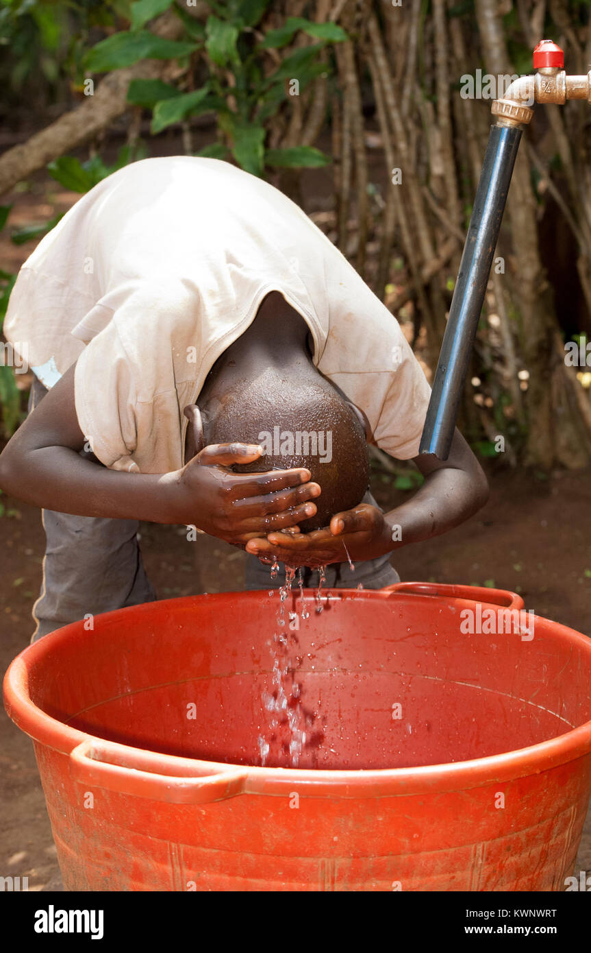 Ragazzo ruandese lavando il suo volto in acqua pulita proveniente dal tubo in borgo rurale. Foto Stock