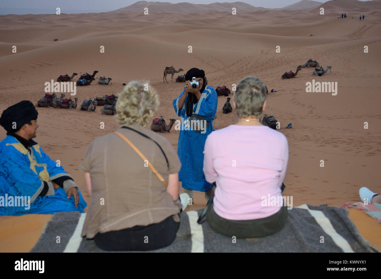 I turisti aventi la loro fotografia scattata da un riff guida su un escursione in cammello alle dune di sabbia di Merzouga, Marocco, Africa del Nord Foto Stock