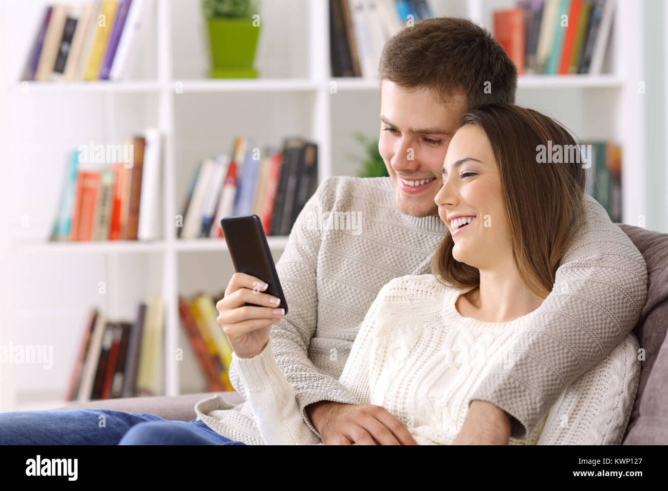 Coppia felice la visione di contenuti multimediali su uno smart phone seduto su un divano a casa Foto Stock