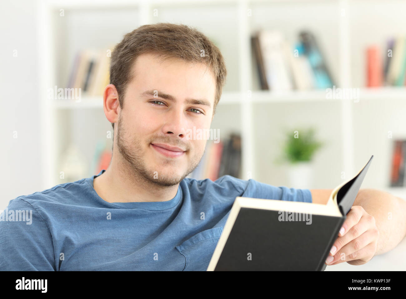 Vista frontale - Ritratto di un uomo che legge un libro guardando seduto su un divano a casa Foto Stock