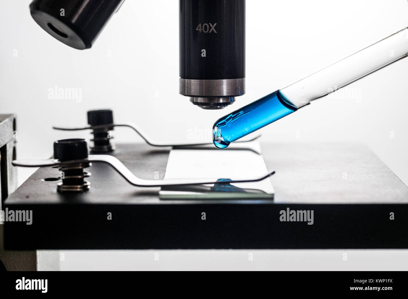 Pipetta contagocce, ponendo una sostanza blu goccia su un microscopio e vetro per microscopio diapositiva, closeup, sfondo bianco macro retroilluminato Foto Stock