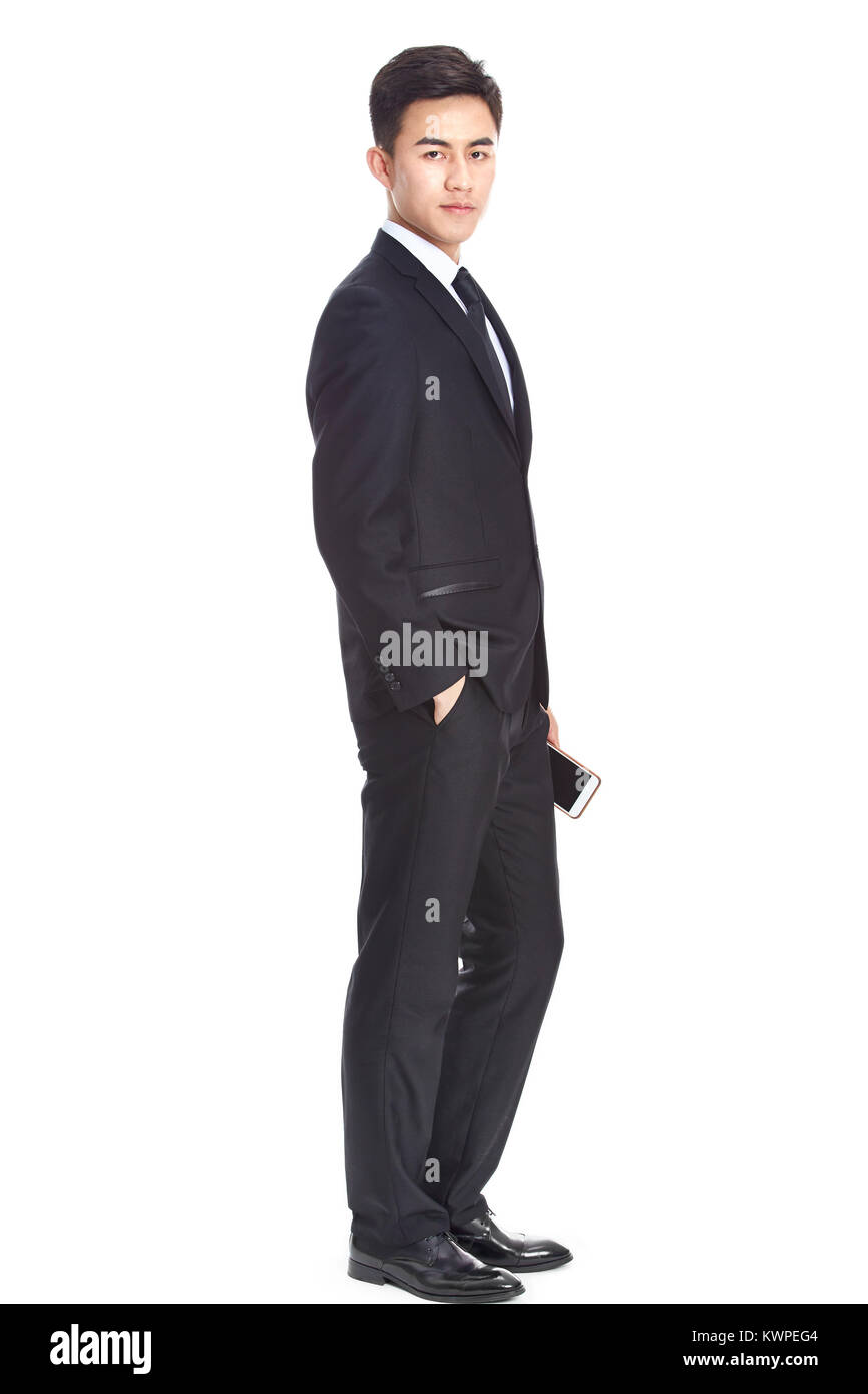 Studio ritratto di una giovane asian business man, il cellulare in mano, guardando la telecamera, vista laterale, isolato su sfondo bianco. Foto Stock