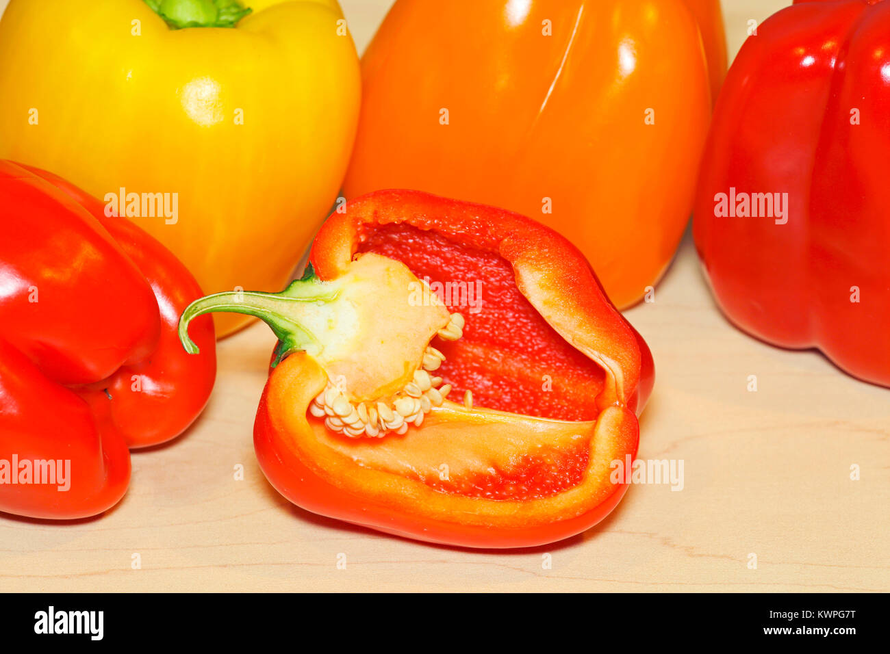 Organici di rosso, giallo e arancione il peperone paprika su legno di acero bordo, vicino con un peperone tagliato a metà. Foto Stock