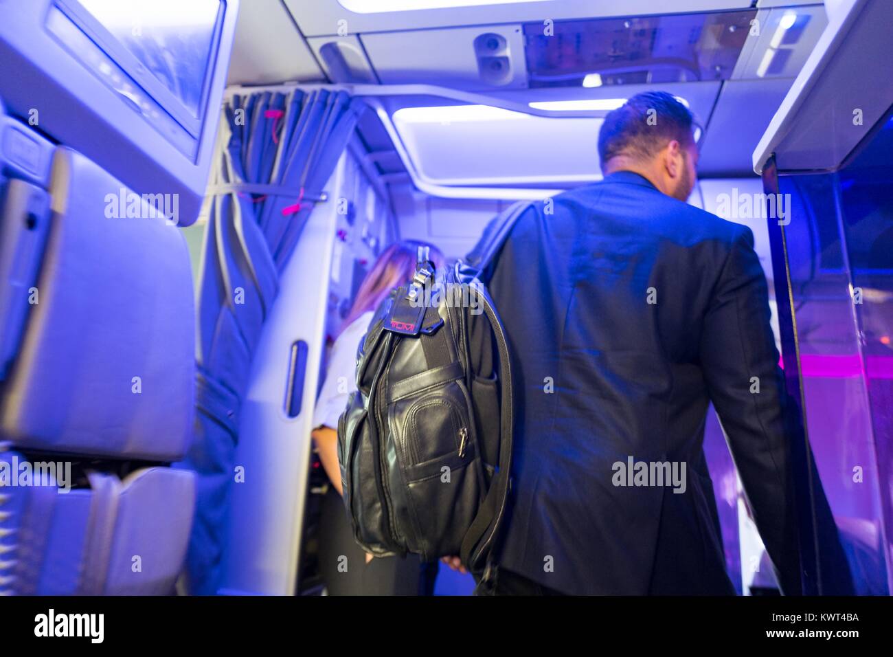 Un imprenditore che indossa una tuta e una valigia Tumi pannelli a Virgin America aereo, con distintivi viola 'mood' illuminazione visibile, all'Aeroporto Internazionale di San Francisco (SFO), San Francisco, California, 13 settembre 2017. Foto Stock