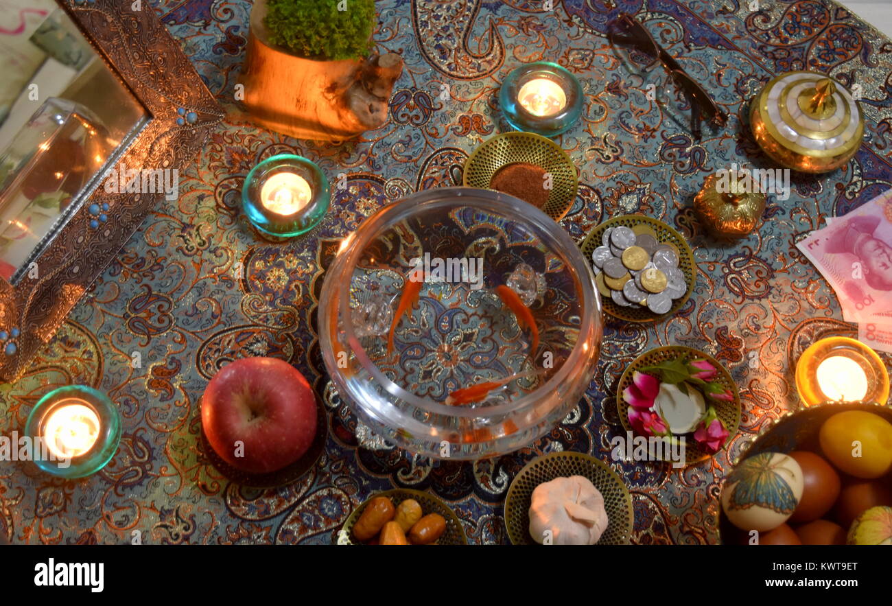 Tabella a lume di candela sparsi per il persiano iraniano nuovo anno celebrazione Norouz compresi artigianato tradizionale di prodotti tessili e il pesce dorato in una ciotola Foto Stock