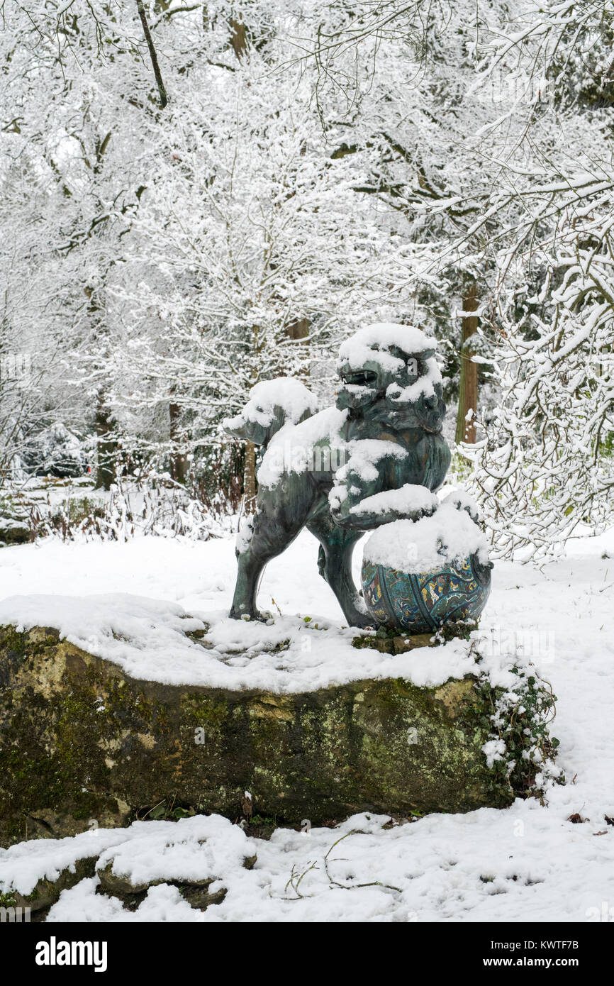 Cinese cane pippo statua in bronzo e inverno alberi nella neve in dicembre a Batsford Arboretum, Cotswolds, Moreton-in-Marsh, Gloucestershire, Inghilterra Foto Stock