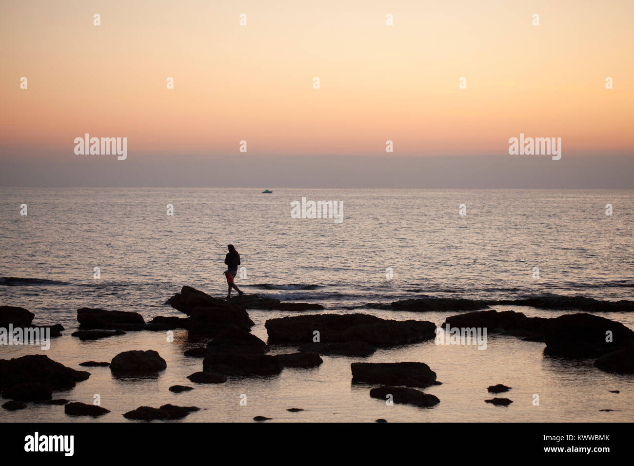 Un pescatore pesci sulle rocce a Livorno il lungomare al tramonto, Toscana, Italia Foto Stock