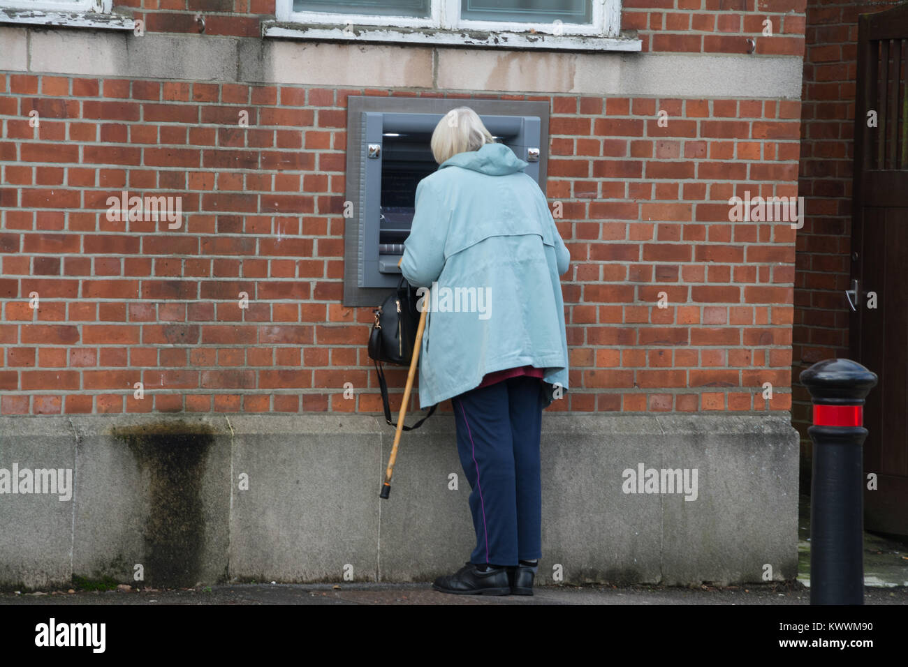 Donna anziana con un bastone da passeggio con un esterno di bancomat (ATM, Bancomat) presso una banca Foto Stock