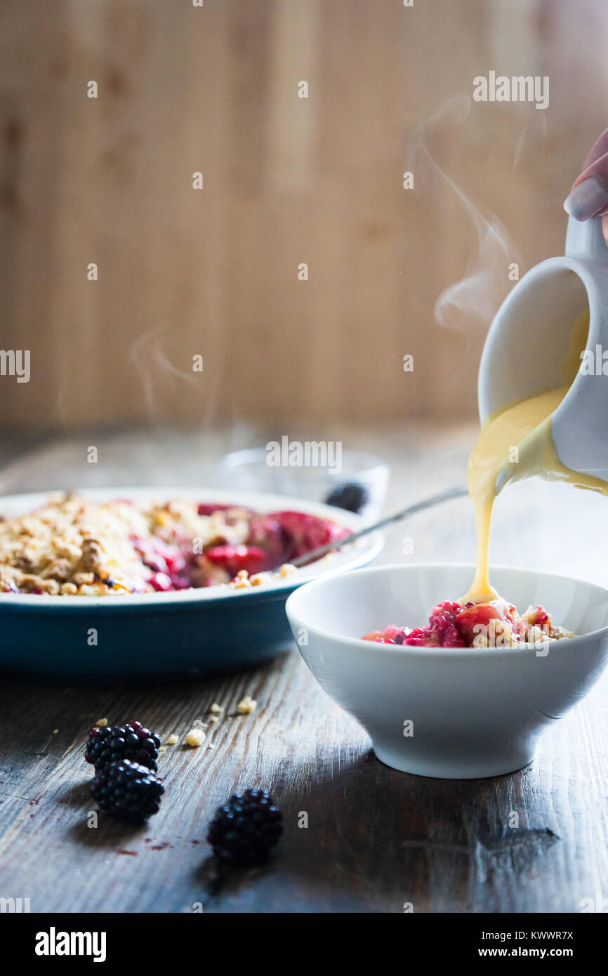 Crema pasticcera calda che viene versato nel corso della cottura a vapore la frutta crumble Foto Stock