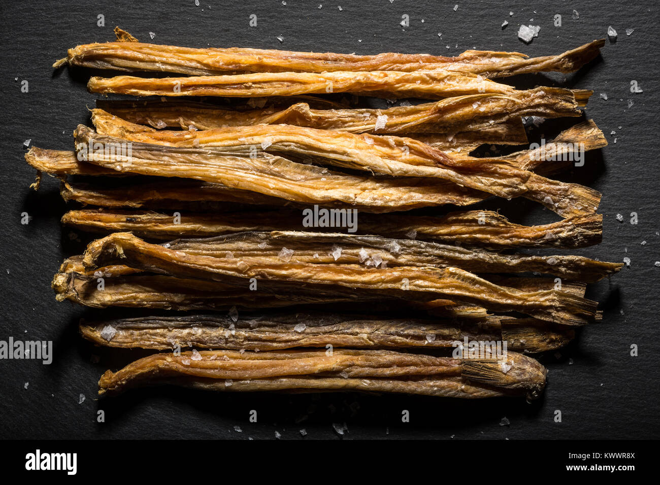 Un mazzetto di pesce essiccati noti come Bumalo giacciono su una spruzzata di ardesia con scaglie di sale. Foto Stock