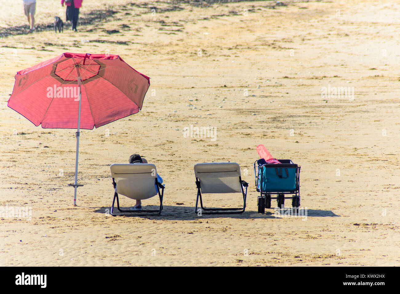 Un uomo relax su un lettino su di una spiaggia di sabbia in una giornata di sole in Westgate, Inghilterra, Regno Unito. Un cane e due escursionisti può essere visto in lontananza. Foto Stock