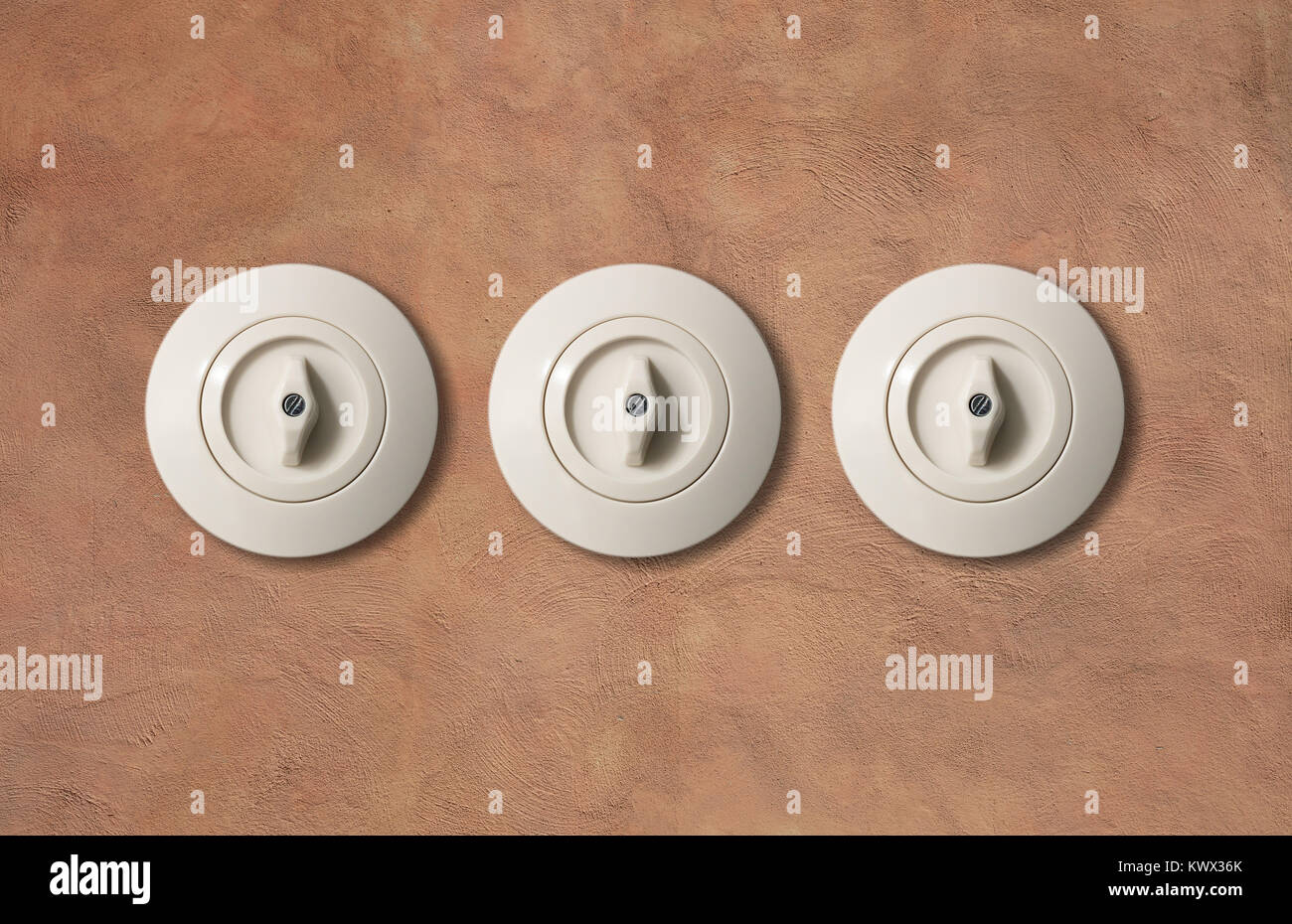 Tre interruttori vintage rotondo con pulsante da isolato di porcellana sulla luce marrone parete in stucco. Close up, dettaglio. Foto Stock