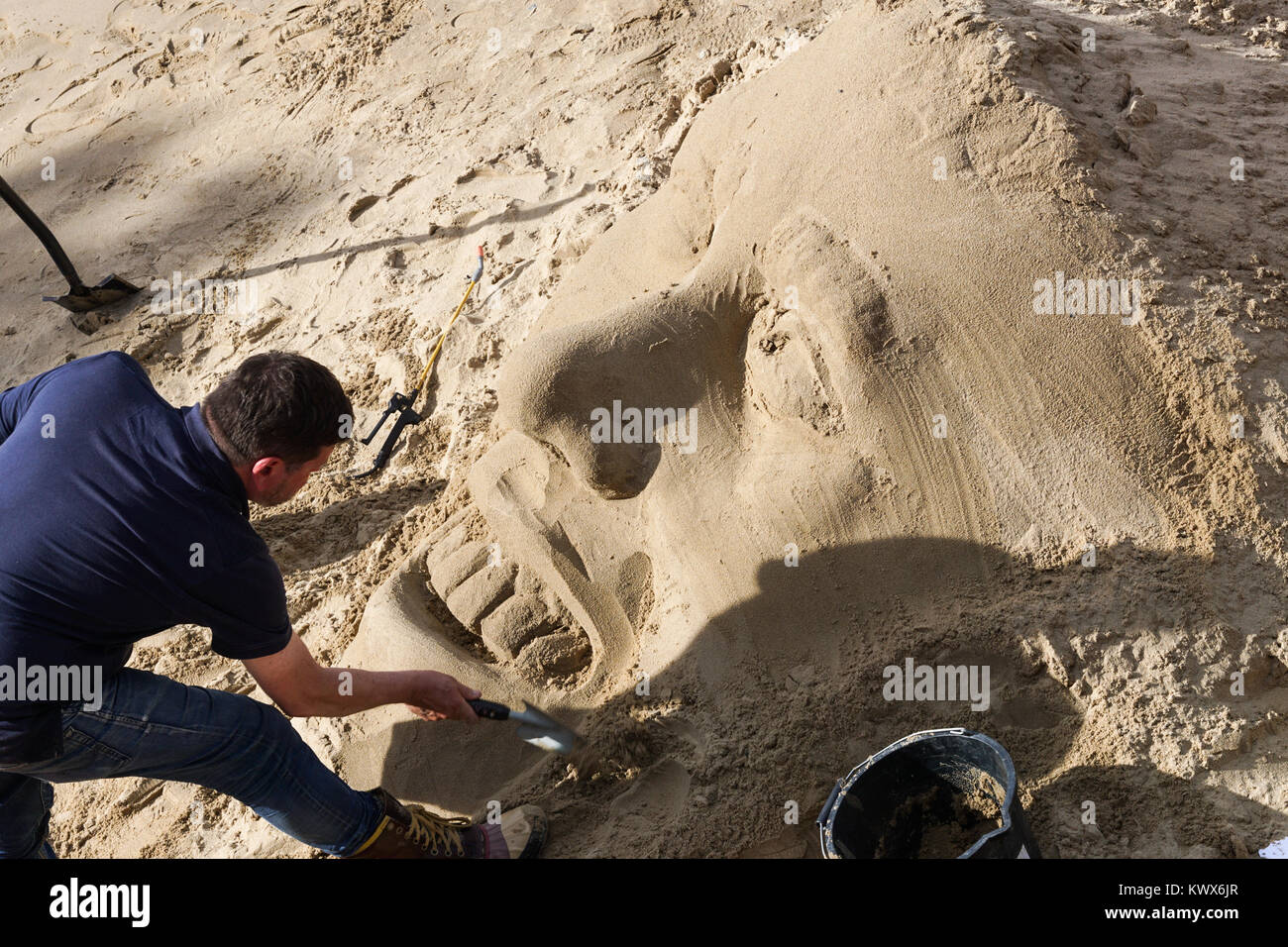 Scultore di sabbia lavorando su una testa nella sabbia sulla South Bank di Londra. Foto Stock