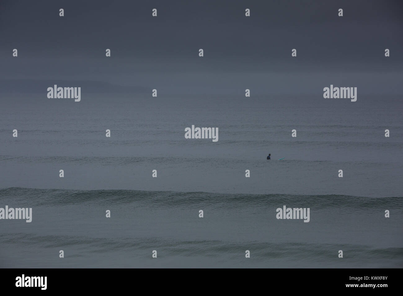 Dark broody cieli di un singolo surfer su un moody giornata grigia in North Devon Foto Stock